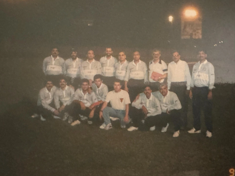 A team poses in two rows outdoors at night, most wearing white sports shirts.
